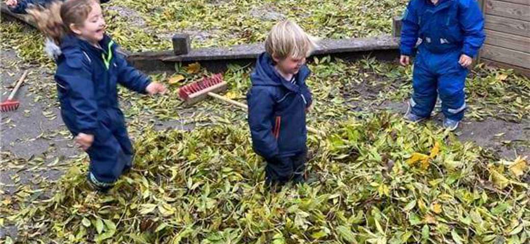 Børn har haft travlt med at feje blade på legepladsen sammen - og nu skal der hoppes og kastes blade op i luften