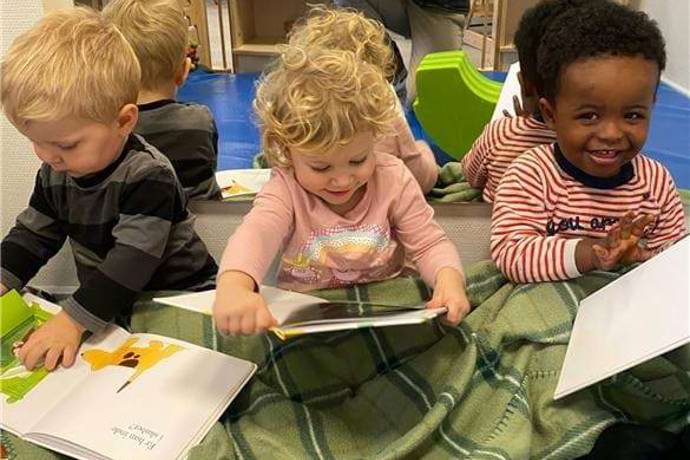 Vuggestuebørn sidder varmt under tæppet og læser i deres ynglingsbøger