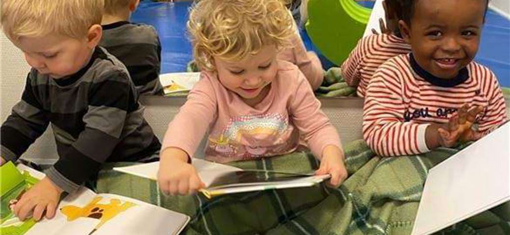 Vuggestuebørn sidder varmt under tæppet og læser i deres ynglingsbøger