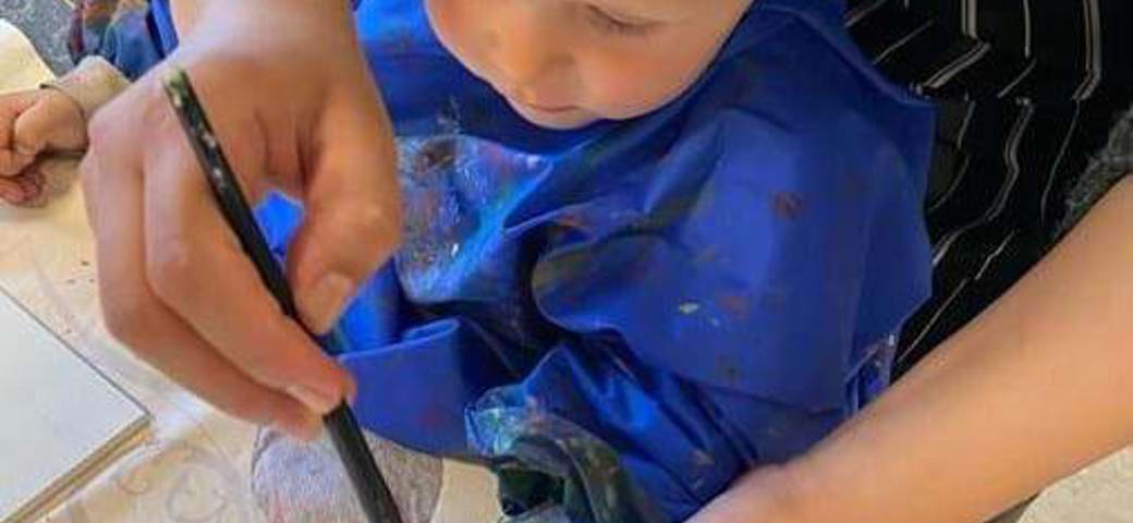 Pædagog hjælper barn med at lave et håndaftryk med sølvmaling - det bliver en gave til forældrene