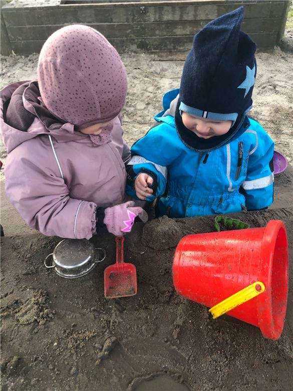 To børn leger med sand og mudder på legepladsen