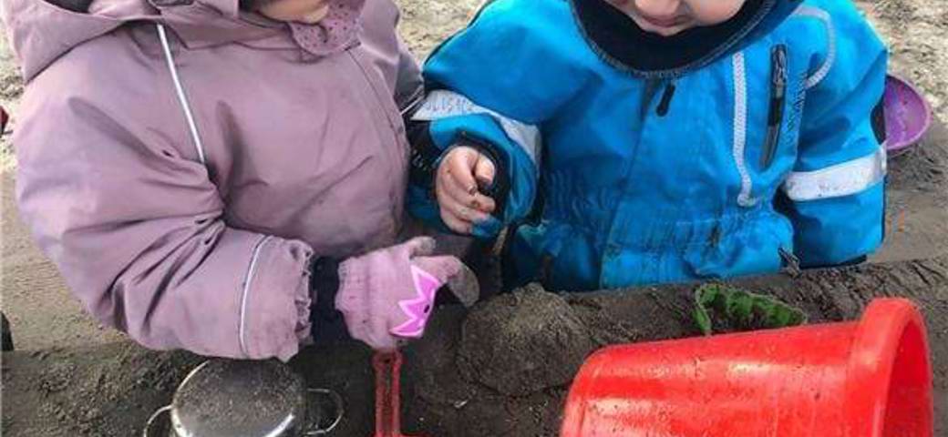 To børn leger med sand og mudder på legepladsen
