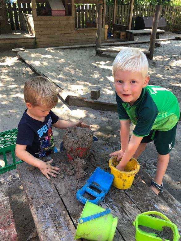 To børn er i gang med at opdage hvordan man blander vand og sand til mudder man kan bygge med