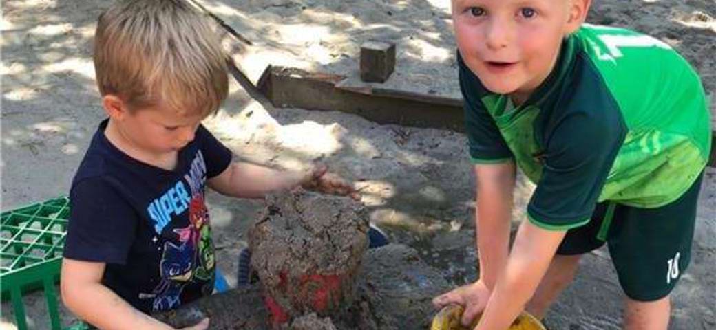 To børn er i gang med at opdage hvordan man blander vand og sand til mudder man kan bygge med